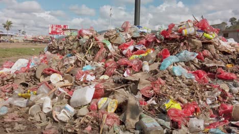 Pile-of-trash-pan-to-reveal-street-in-tropical-town-with-people-and-vehicles