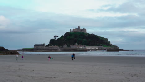 Niños-Jugando-Con-Una-Cometa-En-La-Playa-De-Marazion-En-Cornualles-Con-El-Castillo-Medieval-Inglés-Y-La-Iglesia-Del-Monte-De-San-Miguel-Detrás