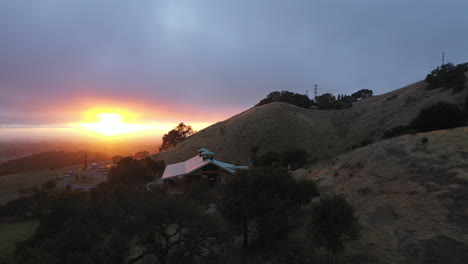 Aerial-flyover-of-a-grassy-ridge-revealing-a-beautiful-sunset-over-the-rebuilding-Paradise-Ridge-Winery-after-the-2017-Tubbs-wildfires-in-Santa-Rosa,-California