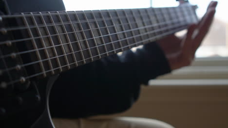 Man-Practising-a-vintage-black-electric-guitar,-rehearsing-chords,-solos-and-octaves-in-a-natural-light-environment.