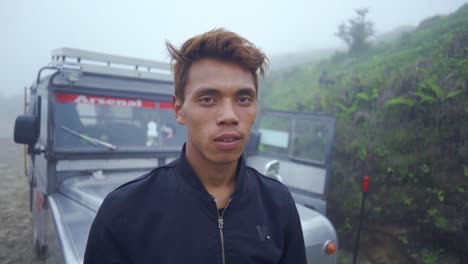 Lonely-and-Upset-young-Asian-male-driver-on-mountain-road-at-foggy-morning-looking-at-camera,-land-rover