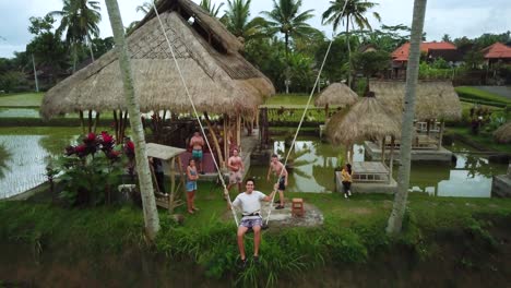 Toma-De-Un-Dron-De-Un-Turista-Disfrutando-De-Un-Columpio-Entre-Dos-Cocoteros-Que-Se-Balancea-Sobre-Algunas-Terrazas-De-Arroz-En-Bali,-Indonesia