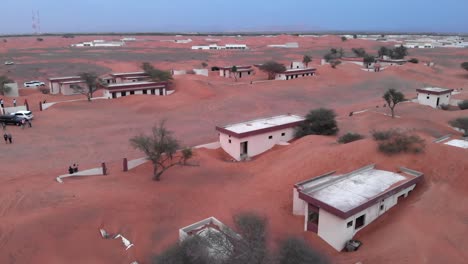 Aerial-view-over-tourists-in-abandoned-village-covered-in-sand-in-the-desert-of-Dubai,-United-Arab-Emirates