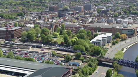 Tracking-aerial-view-of-a-commuter-train-leaving-Maidstone-East-station-and-crossing-the-River-Medway-in-Maidstone,-Kent