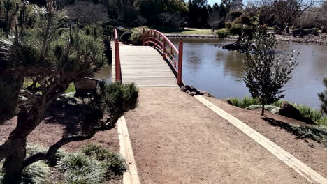 Tiro-Panorámico,-Pasarela-Al-Puente-Rojo-Sobre-El-Estanque,-Ju-Raku-En-Jardín-Japonés,-Toowoomba-Australia