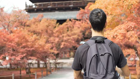 Tipo-Caminando-Hacia-Un-Santuario-Cepillándose-Las-Manos-En-Las-Hojas-Naranjas-De-Otoño-En-Kyoto,-Japón-Iluminación-Suave-Cámara-Lenta-4k