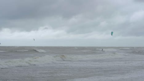 Kite-surfing-surfers-sailing-on-the-big-Baltic-sea-waves-at-Liepaja-Karosta-beach,-overcast-autumn-day,-slow-motion-wide-shot