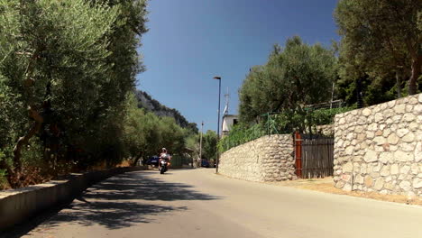 Motorrad-Und-Auto,-Die-Auf-Einer-Von-Bäumen-Gesäumten-Straße-An-Der-Amalfiküste-Mit-Blauem-Himmel,-Italien,-Vorbeifahren