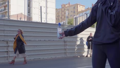 Vista-De-Cerca-Del-Voluntario-Sosteniendo-La-Botella-De-Agua,-Mientras-Los-Corredores-De-Maratón-Pasan-Corriendo-Junto-A-Ella