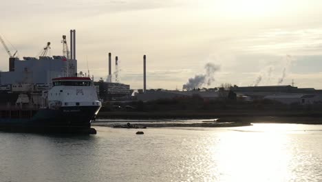 Aerial-slider-profile-shot-of-a-ship-loading-on-the-Swale-Estuary,-with-industry-surrounding