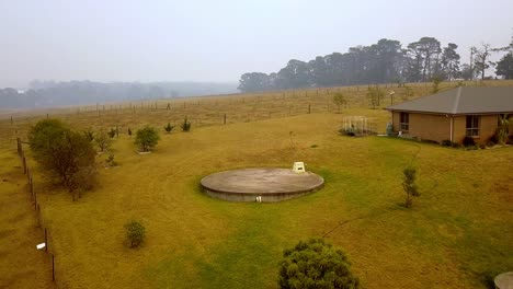 Home-ranch-in-fire-danger-from-nearby-eucalyptus-forest-blaze,-Aerial-drone-flyover-reveal-shot