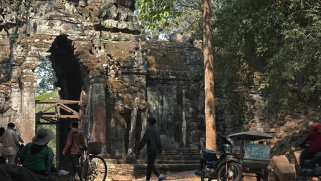 Mittlerer-äußerer-Zeitraffer-Des-Alten-Tores,-Das-Zum-Tempel-Angkor-Wat-Führt,-Mit-Menschen-Und-Verkehr,-Die-Durch-Ihn-Hindurchgehen,-Und-Einer-Dame,-Die-Tagsüber-Mit-Dem-Rücken-Zur-Kamera-In-Einem-Sonnenhut-Sitzt