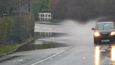 Schwarzes-Auto,-Das-Durch-Stürmische,-überflutete-Straßeneckenkurve-Uk-Spritzt