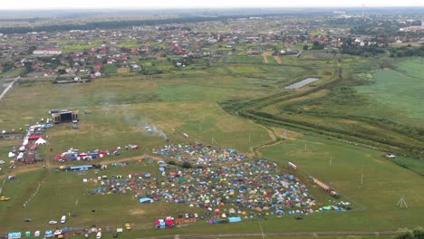 Vista-Aérea-De-Carpas-Multicolores-Colocadas-En-Un-Campo-En-Un-Festival-De-Música-Con-La-Ciudad-En-Segundo-Plano