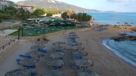 Ufer-Des-Plaka-Beach-Resort-Im-östlichen-Teil-Der-Insel-Mit-Stühlen,-Sonnenschirmen-Und-Einem-Volleyballnetz,-Luftdrohnen-dolly-in-aufnahme