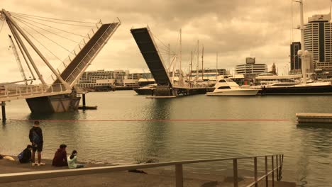 An-overcast-sky-casts-an-orange-hue-over-the-bascule-bridge-opening-upwards-as-a-few-tourists-look-on