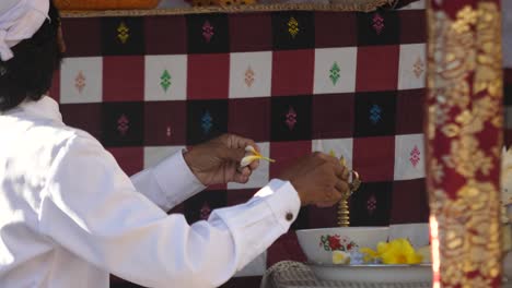 Sacerdote-Hindú-Prepara-Una-Ofrenda-Con-Flores-De-Color-Amarillo-Brillante-En-Un-Altar-En-Un-Templo-De-Bali,-Indonesia