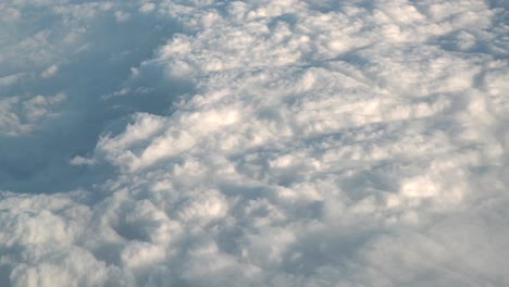 Clouds-from-high-above-in-plane-flight-aerial-motion,-sun-light-and-shadows-on-condensation,-weather-symbol