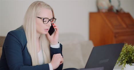 Young-Businesswoman-Talking-On-Mobile-Phone-Using-Laptop-Computer