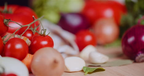 Nahaufnahme-Von-Verschiedenen-Gemüsesorten-Auf-Dem-Tisch,-Die-Frische-Kirschtomaten-Rotieren,-Karotten,-Rote-Zwiebeln-Und-Knoblauch