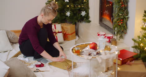 Woman-Wrapping-Christmas-Present-By-Fireplace-At-Home-6