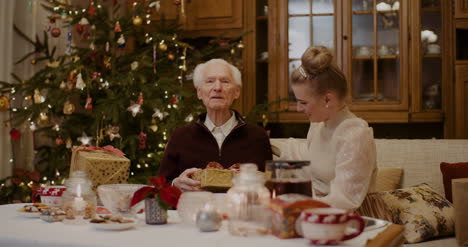 Woman-Giving-Christmas-Present-To-Grandfather-At-Home