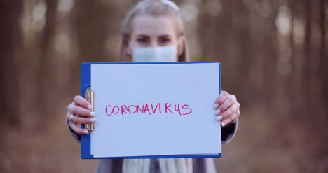 Mujer-Con-Máscara-Protectora-Con-Inscripción-De-Coronavirus-En-Manos-En-Bosque