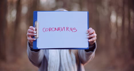 Frau-Mit-Schutzmaske-Mit-Coronavirus-Aufschrift-In-Den-Händen-Im-Wald-2