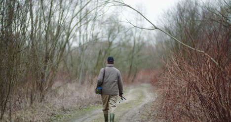Man-Holding-Fishing-Rod-Walking-Amidst-Bare-Trees-5