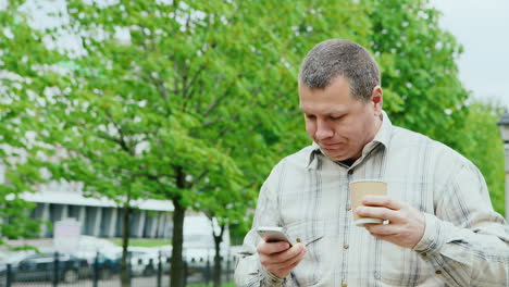 Brutal-Man-Walking-In-The-Park-Using-A-Mobile-Phone-And-Drinking-Coffee-From-A-Paper-Cup