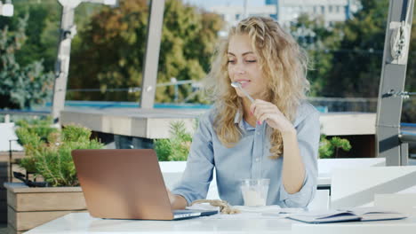 Young-Business-Woman-Working-In-A-Cafe-On-The-Summer-Ground-He-Eats-Ice-Cream-Uses-A-Laptop