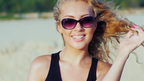 Eine-Attraktive-Junge-Frau-Mit-Sonnenbrille-Posiert-Lächelnd-In-Die-Kamera-Am-Strand