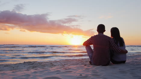Junges-Romantisches-Paar,-Das-Am-Strand-Sitzt-Und-Den-Sonnenuntergang-Bewundert