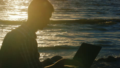 Young-Man-Working-With-A-Laptop-By-The-Sea-At-Sunset