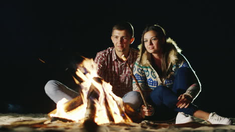 Man-And-Woman-Relaxing-Evening-Around-The-Campfire-Roast-Marshmallows-On-Sticks-Fire
