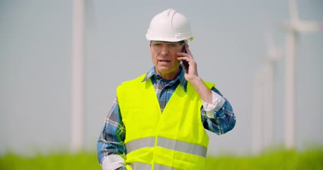 Engineer-Talking-On-Mobile-Phone-Against-Windmills-Farm