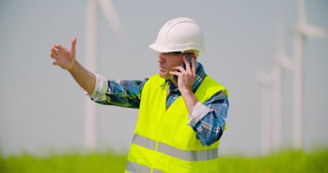 Angry-Engineer-Talking-On-Mobile-Phone-Against-Windmills-Farm-3