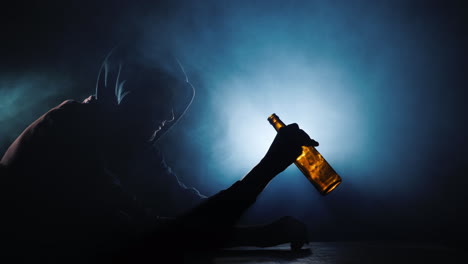 Silhouette-Of-A-Man-Sitting-With-An-Empty-Bottle-Of-Alcohol-In-His-Hand