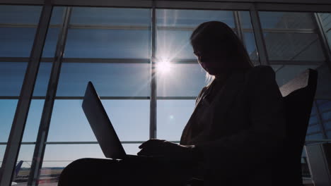 Silhouette-Eines-Mannes-Mit-Einem-Laptop-In-Der-Nähe-Eines-Großen-Fensters-Im-Flughafenterminal