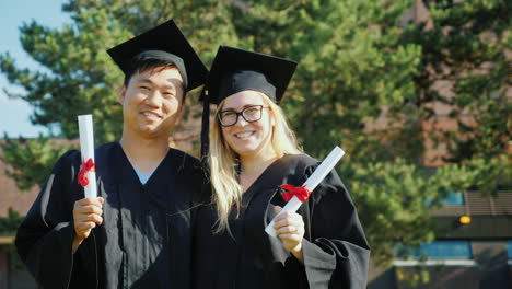 A-Portrait-Of-Two-Graduates---An-Asian-Man-And-A-Caucasian-Woman-In-The-Clothes-And-Caps-Of-The-Grad