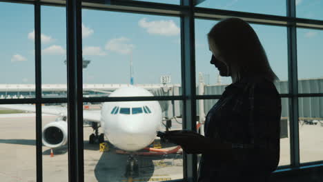 Silhouette-Einer-Geschäftsfrau-Am-Fenster-Eines-Flughafenterminals-Benutzt-Ein-Smartphone
