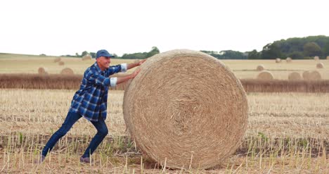 Smiling-Farmer-Rolling-Hay-Bale-And-Gesturing-In-Farm-4