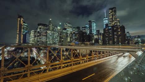 Traffic-Over-The-Famous-Brooklyn-Bridge-At-Night-Against-The-Backdrop-Of-The-Skyscrapers-Of-Manhatta