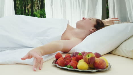 A-Young-Woman-Wakes-Up-On-A-Lounger-Covered-With-Curtains-Near-Her-A-Plate-Of-Fruit-Gorgeous-Romanti
