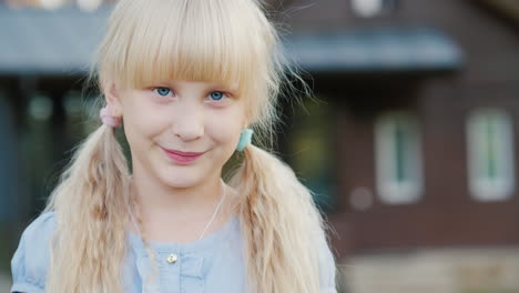 Porträt-Eines-Blonden-Mädchens-6-Jahre-Alt,-Das-In-Die-Kamera-Lächelt,-Es-Steht-Im-Hintergrund-Seines-Hauses