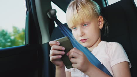 Technologie-Auf-Der-Straße-Das-Mädchen-Ist-6-Jahre-Alt-Und-Spielt-Auf-Einem-Smartphone-Sie-Fährt-Einen-Autositz-4k-V