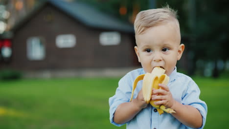 Cheerful-1-Year-Old-Baby-Is-Eating-A-Banana-It's-Standing-On-The-Back-Of-The-House-4k-Video