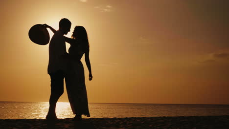 Silhouette-Of-Couple-In-Love-They-Look-At-Each-Other-Hug-And-Kiss-At-Sunset-Against-The-Background-O