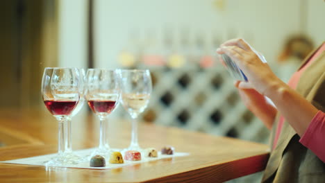 Eine-Frau-Fotografiert-Eine-Reihe-Von-Gläsern-Und-Eine-Schöne-Süßigkeitenweinprobe-Mit-Süßigkeiten-Und-Weintour-Wine