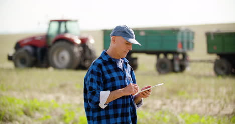 Farmer-Using-Digital-Tablet-While-Looking-At-Tractor-In-Farm-4